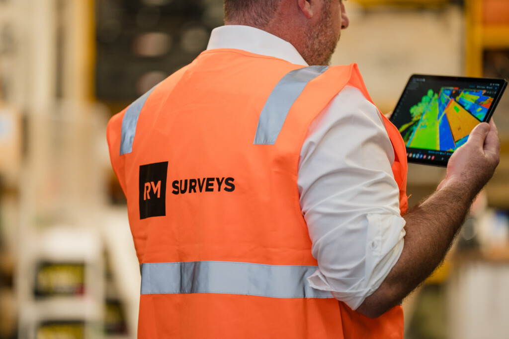 Surveyor wearing a high-visibility RM Surveys vest using a tablet to view 3D mapping data.