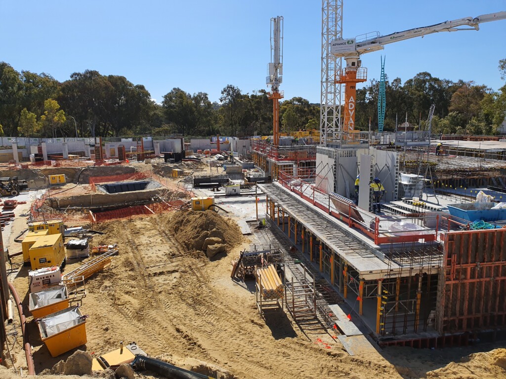 Aerial view of a large, active construction site showing deep excavation, crane operations, and multiple structures under development.