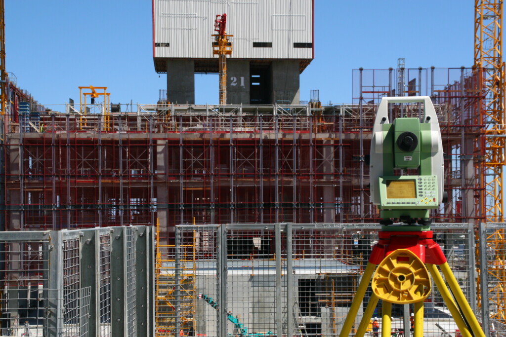 Total station set up on an active construction site with scaffolding and tower crane in the background, used for structural monitoring and deformation measurement