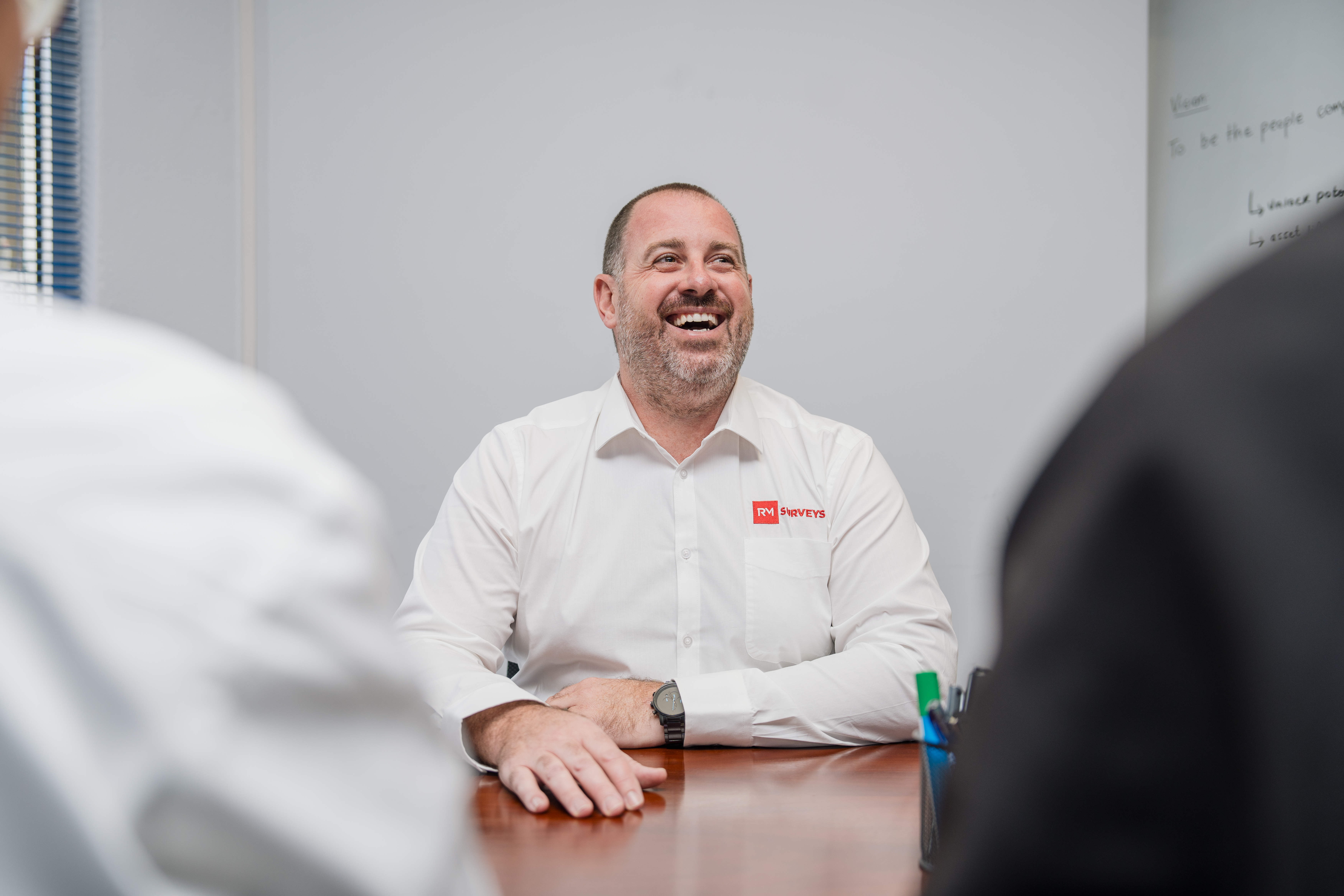 RM Survey employee smiling during a meeting, seated at a table in a professional office setting