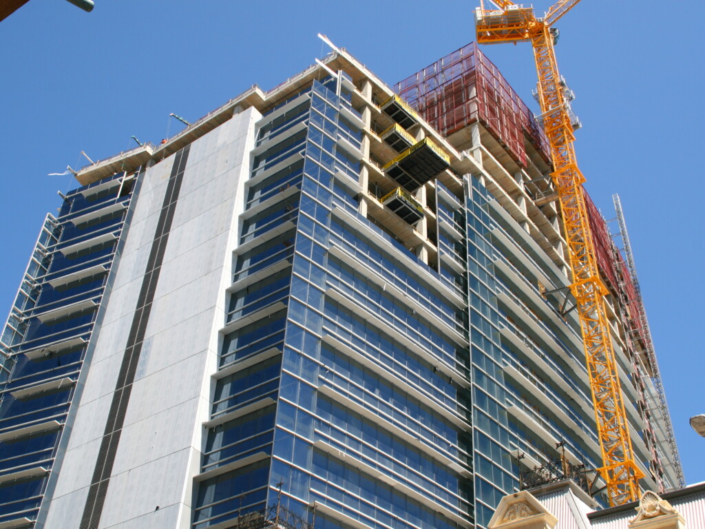 High-rise building under construction in an urban setting with tower crane, illustrating the complex environments where automatic deformation monitoring system is essential.